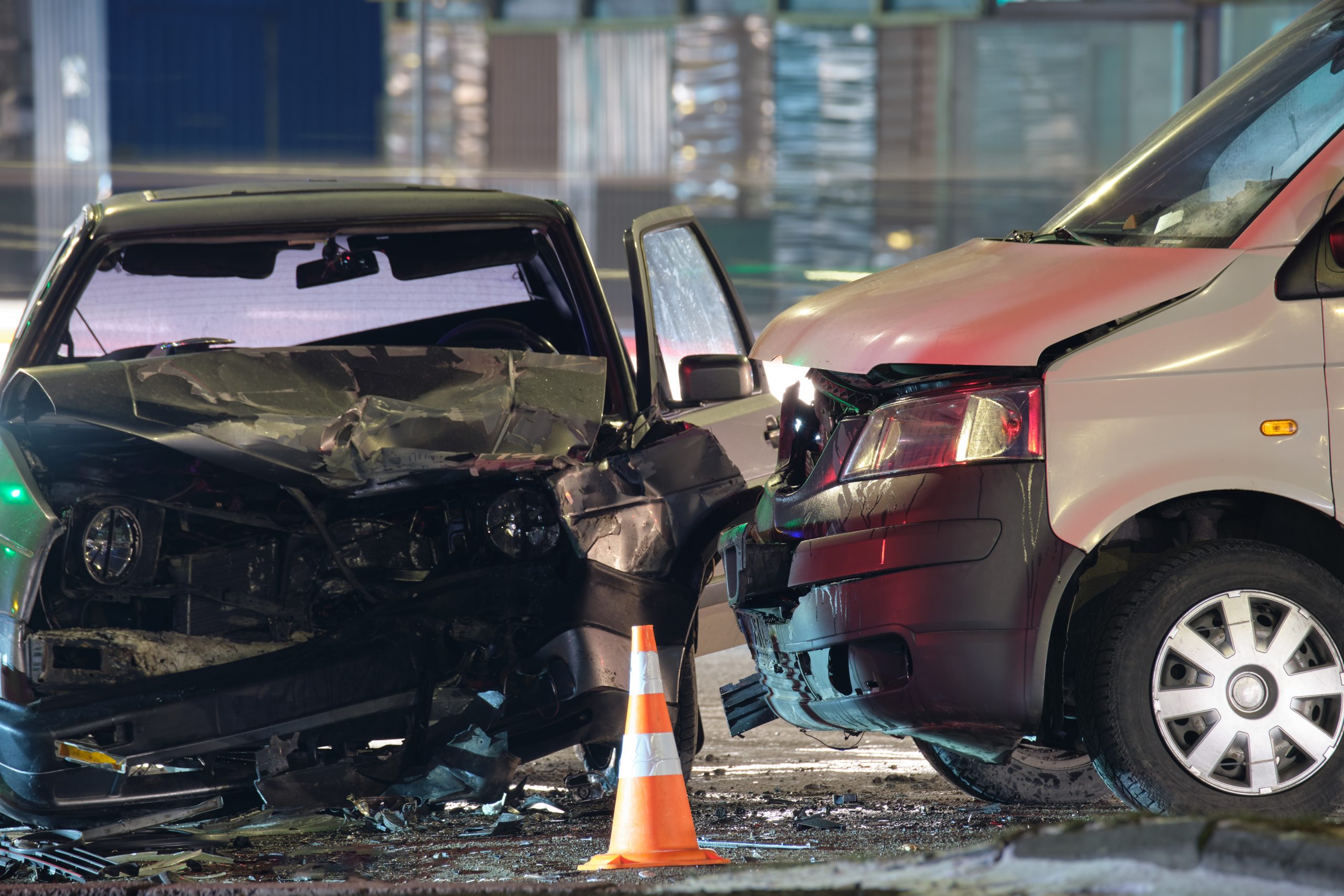 Two cars collide head-on with extensive front-end damage, orange cones nearby at the accident scene.